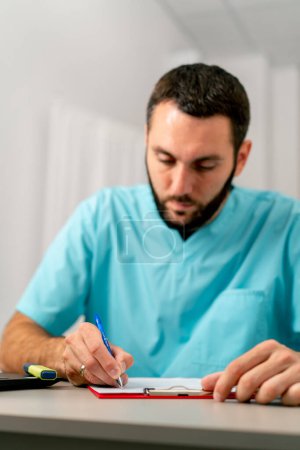 Photo for Close-up shot of a concentrated doctor with a beard filling out documents in his office in a hospital - Royalty Free Image
