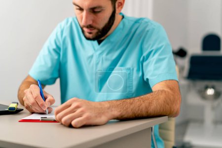 Téléchargez les photos : Gros plan d'un médecin concentré avec une barbe remplissant des documents dans son bureau dans un hôpital - en image libre de droit
