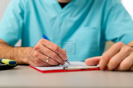 Photo for Close-up shot of a male doctor's hand with a ring on his finger filling out a patient's medical history - Royalty Free Image