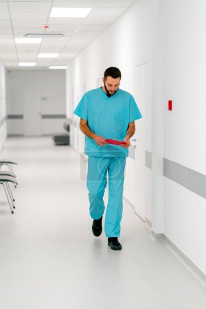 Foto de Un médico hombre alto con barba camina por el pasillo del hospital con una carpeta de documentos - Imagen libre de derechos