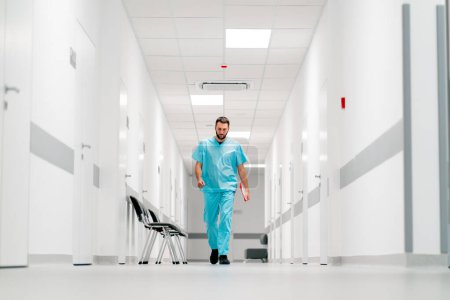 Téléchargez les photos : Un grand médecin avec une barbe marche le long du couloir de l'hôpital avec un dossier de documents - en image libre de droit
