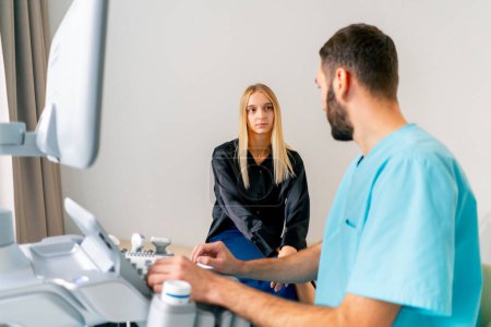 Foto de Una paciente se sienta en una camilla en la sala de diagnóstico por ultrasonido después del procedimiento y escucha atentamente a un médico. - Imagen libre de derechos