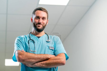 Foto de Retrato de un médico sonriente con barba y un estetoscopio alrededor del cuello en el pasillo de un amplio centro médico - Imagen libre de derechos