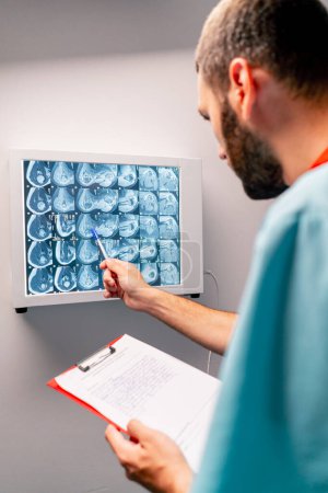 Téléchargez les photos : Le radiologue étudie attentivement l'image IRM sur un tableau spécial décrit ce qu'il a vu et rédige une conclusion de diagnostic - en image libre de droit