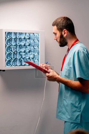 Photo for The radiologist carefully studies the MRI image on special board describes what he saw and writes a diagnosis conclusion - Royalty Free Image