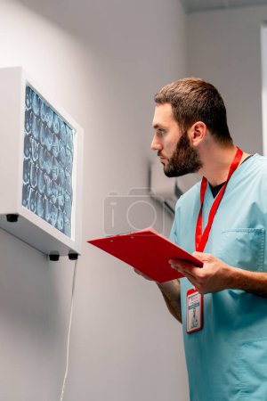 Foto de El radiólogo estudia cuidadosamente la imagen de resonancia magnética en el tablero especial describe lo que vio y escribe una conclusión de diagnóstico - Imagen libre de derechos