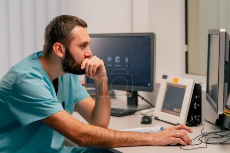 Foto de Médico masculino concentrado se sienta en un monitor de computadora en una habitación para describir imágenes de resonancia magnética y monitorear la condición del paciente - Imagen libre de derechos
