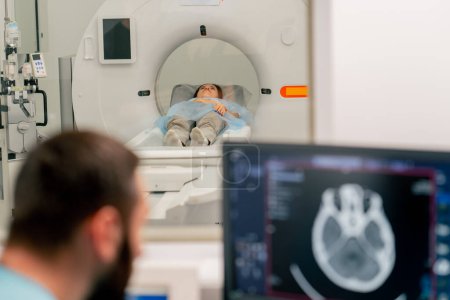 Foto de Un radiólogo se sienta en una mesa detrás de un monitor de computadora y examina una imagen de resonancia magnética durante un examen de un paciente. - Imagen libre de derechos