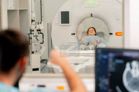Foto de Una niña se acuesta en una máquina de resonancia magnética antes de examinar su cuerpo y el radiólogo le da la orden de prepararse para un diagnóstico - Imagen libre de derechos
