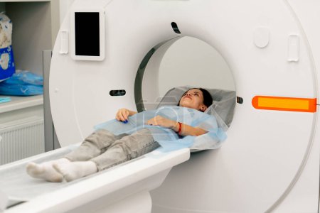 Foto de Una niña con una bata médica yace en un sofá móvil de una máquina de imágenes por resonancia magnética y se prepara para un diagnóstico - Imagen libre de derechos