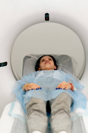 Photo for A girl in a medical gown lies on a movable couch of a magnetic resonance imaging machine and prepares for a diagnosis - Royalty Free Image