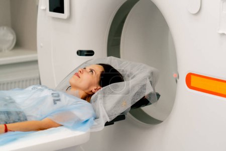 Foto de Una niña con una bata médica yace en un sofá móvil de una máquina de imágenes por resonancia magnética y se prepara para un diagnóstico - Imagen libre de derechos