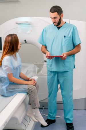 Photo for A radiologist consults a girl patient before undergoing diagnostics using an MRI machine in a medical center - Royalty Free Image
