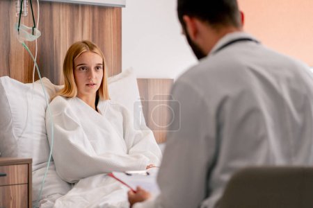 Téléchargez les photos : Une fille malade se trouve dans la chambre d'hôpital et tient sa poitrine avec sa main et une toux près du médecin - en image libre de droit