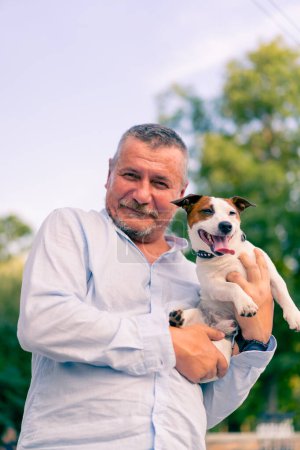 Foto de Retrato de un hombre barbudo adulto sosteniendo su pequeño perro de la raza Jack Russell Terrier cuidando animales amistad - Imagen libre de derechos