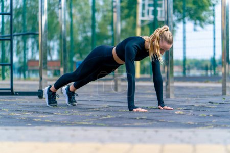 Photo for A sports girl performs a plank exercise to strengthen all muscle groups of the body during a morning workout on the sports ground - Royalty Free Image