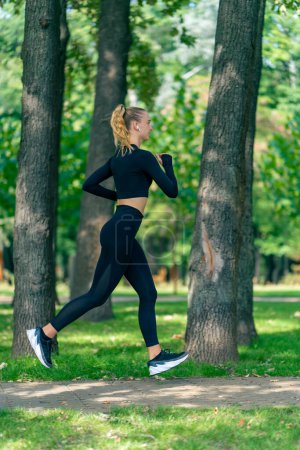 Foto de Una joven en ropa deportiva y auriculares corre en el parque por la mañana para mantener la aptitud física - Imagen libre de derechos