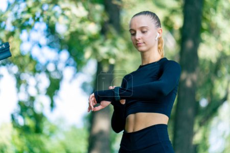 Photo for Portrait of a sporty girl while jogging in the park looking at the sports watch on her hand - Royalty Free Image