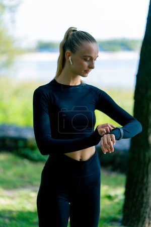 Téléchargez les photos : Portrait d'une fille sportive tout en faisant du jogging dans le parc en regardant la montre de sport sur sa main - en image libre de droit