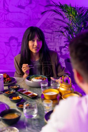 Photo for Portrait of a girl enjoying traditional Korean cuisine with chopsticks in a restaurant with boyfriend on a date - Royalty Free Image