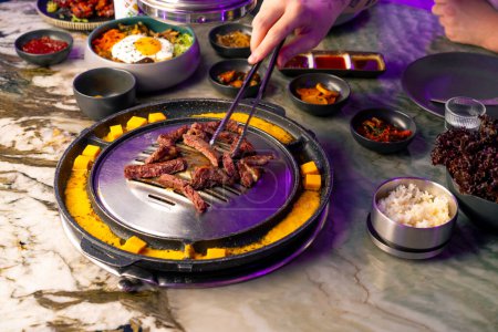 Photo for Close-up of a couple in love at a table having lunch in Korean restaurant picking juicy meat from the grill with tongs - Royalty Free Image