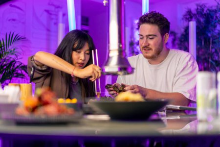 Photo for A couple in love in a korean restaurant with a grill and a hood above the table tastes a variety traditional dishes with chopsticks food concept - Royalty Free Image
