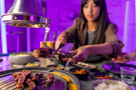 Téléchargez les photos : Gros plan d'un couple amoureux dînant dans un restaurant coréen ramassant de la viande juteuse du gril avec des pinces coupées avec des ciseaux - en image libre de droit