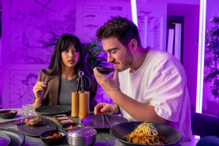 Photo for A couple in love in a korean restaurant with a grill and a hood above the table tastes a variety traditional dishes with chopsticks food concept - Royalty Free Image