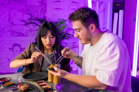 Téléchargez les photos : Un couple amoureux dans un restaurant coréen avec un gril et une hotte au-dessus de la table goûte une variété de plats traditionnels avec des baguettes concept alimentaire - en image libre de droit