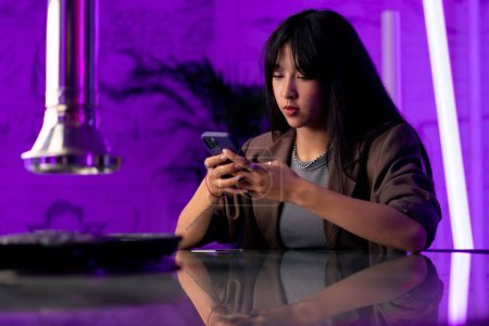 Photo for A young beautiful girl is sitting with a phone in her hands in Korean restaurant waiting for her friend - Royalty Free Image