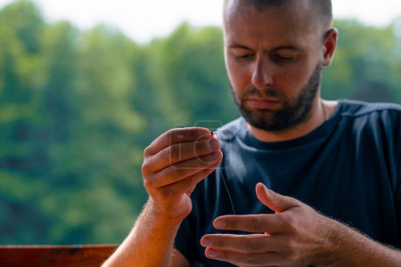 Téléchargez les photos : Un jeune homme ficelle une ligne de pêche ou une mouche sur crochet pour la méthode de style libre mangeoire de pêche - en image libre de droit