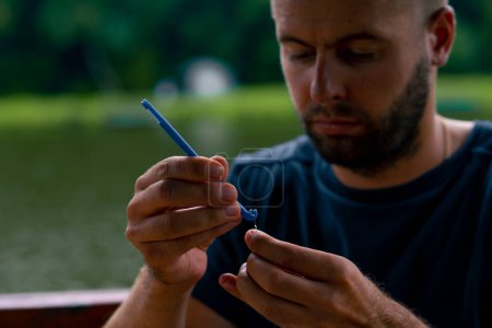 Téléchargez les photos : Un jeune homme ficelle une ligne de pêche ou une mouche sur crochet pour la méthode de style libre mangeoire de pêche - en image libre de droit