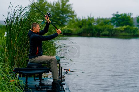 Foto de Pescador lanza una caña de pescar o caña de spinning en el agua mientras está sentado en la orilla del río en el muelle Tire de peces fuera de la pesca deportiva lago - Imagen libre de derechos