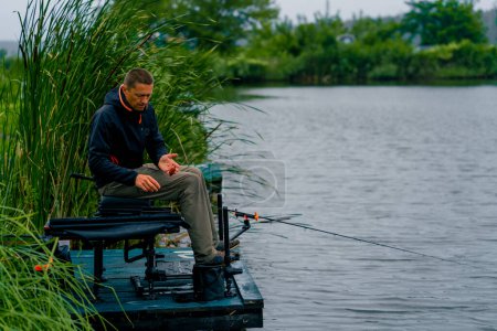 Foto de Pescador con caña de pescar o caña de spinning y herramientas profesionales sentado en la orilla del río Tire de peces de la pesca deportiva lago - Imagen libre de derechos