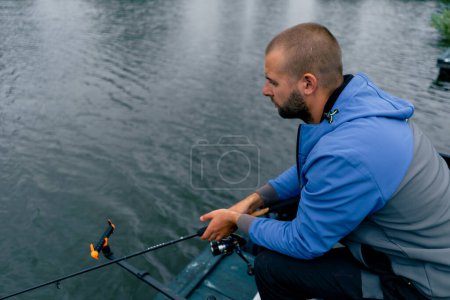 Foto de Pescador con caña de pescar o caña de spinning y herramientas profesionales sentado en la orilla del río Tire de peces de la pesca deportiva lago - Imagen libre de derechos