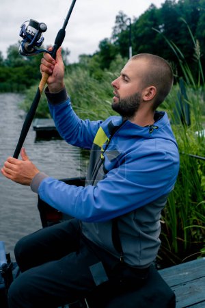Téléchargez les photos : Pêcheur avec canne à pêche ou canne à pêche et outils professionnels assis sur le bord de la rivière Sortir le poisson de la pêche sportive du lac - en image libre de droit