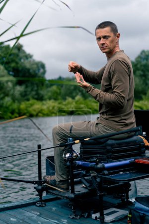 Téléchargez les photos : Portrait d'un pêcheur sérieux enfilant un appât sur le crochet de la canne à pêche pour attraper des poissons de rivière - en image libre de droit