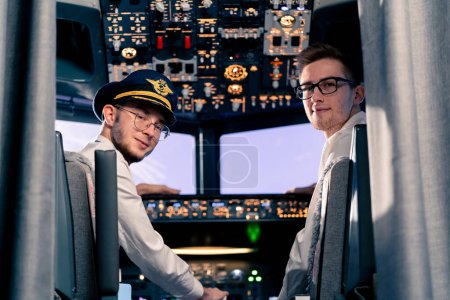 Téléchargez les photos : Portrait de jeunes capitaines souriants de pilotes d'avion en uniforme préparant le vol dans le poste de pilotage d'un simulateur de vol - en image libre de droit
