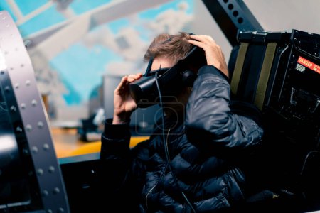 Foto de Un tipo se sienta en un simulador de vuelo de un avión militar antes del inicio del vuelo pone gafas de realidad virtual de entretenimiento - Imagen libre de derechos