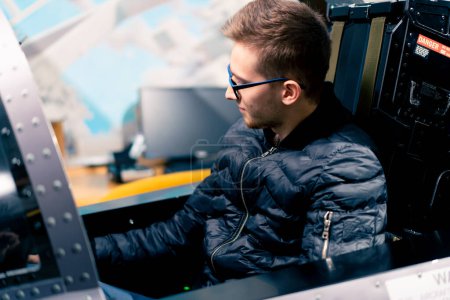 Foto de Un joven se sienta en un simulador de vuelo de un avión militar antes del inicio de un vuelo virtual de entretenimiento - Imagen libre de derechos