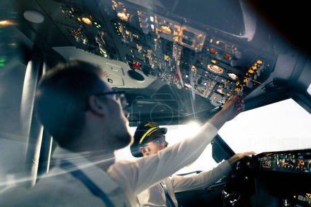 Téléchargez les photos : Jeunes pilotes dans le poste de pilotage de l'avion contrôlent le transport aérien pendant le vol le soleil brille de fenêtre dans le simulateur de distance lointaine - en image libre de droit