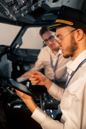 Foto de Pilotos en la cabina del avión cerca del panel de control con una tableta en sus manos discutir la ruta antes del inicio del simulador de vuelo - Imagen libre de derechos