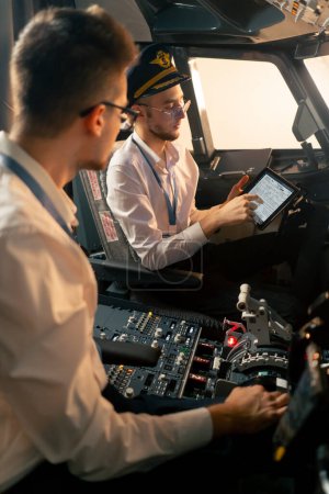 Téléchargez les photos : Les pilotes dans le poste de pilotage de l'avion près du tableau de commande avec une tablette dans leurs mains discutent de la route avant le début du simulateur de vol - en image libre de droit
