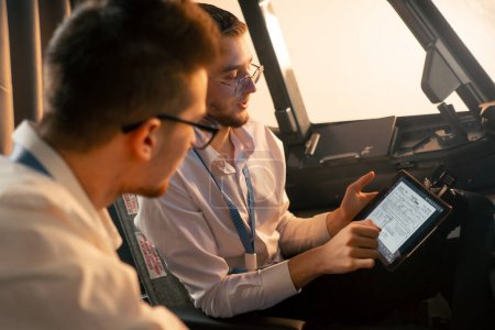 Photo for Pilots in the cockpit of the plane near the control panel with a tablet in their hands discuss the route before the start of flight simulator - Royalty Free Image
