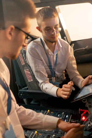 Foto de Pilotos en la cabina del avión cerca del panel de control con una tableta en sus manos discutir la ruta antes del inicio del simulador de vuelo - Imagen libre de derechos