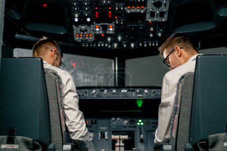 Foto de Visión trasera de los pilotos en la cabina de un avión durante el control de vuelo en el simulador de vuelo de la zona de turbulencia - Imagen libre de derechos
