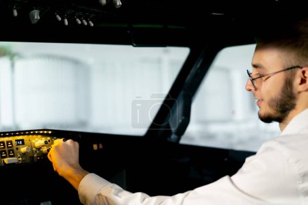 Téléchargez les photos : Le jeune commandant appuie sur les boutons du tableau de commande pour démarrer le simulateur de vol gros plan du moteur de l'avion - en image libre de droit