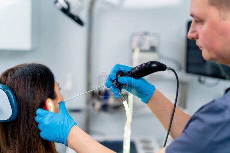 Téléchargez les photos : Un médecin ORL effectue une endoscopie sur l'oreille d'un patient en clinique tenant un appareil professionnel dans sa main - en image libre de droit