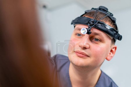 Téléchargez les photos : Portrait d'un médecin ORL avec un projecteur professionnel examinant un patient dans le bureau de la clinique - en image libre de droit