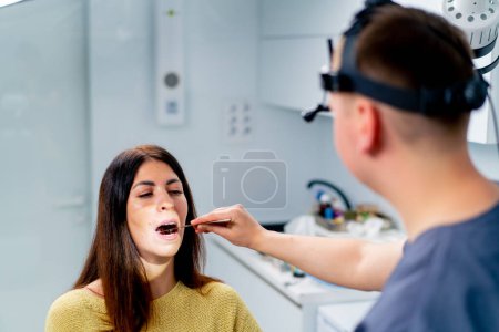 Foto de El médico otorrinolaringólogo examina al paciente en el consultorio de la clínica, comprueba los conductos auditivos de la cavidad oral y nasal con instrumentos profesionales - Imagen libre de derechos